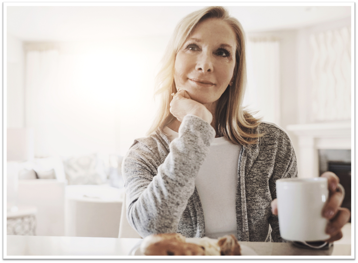 An older woman looking deep in thought drinking from a mug
